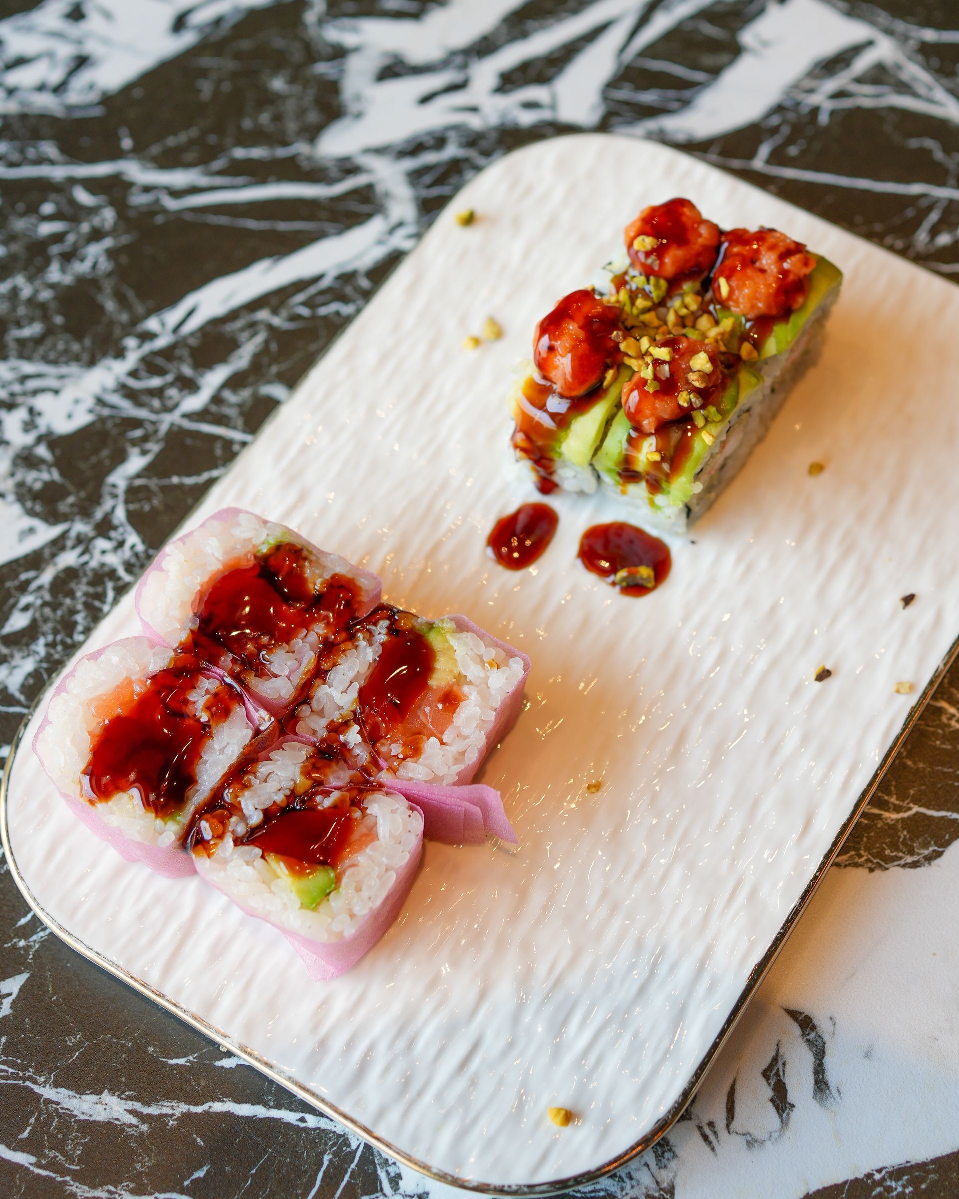 Due piccoli quadratini di dessert su un piatto bianco, irrorati con salsa rossa e guarniti con frutta secca.