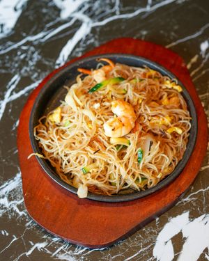 Spaghetti con gamberi saltati in padella in una ciotola nera su una tovaglietta rossa, sopra un tavolo di marmo.