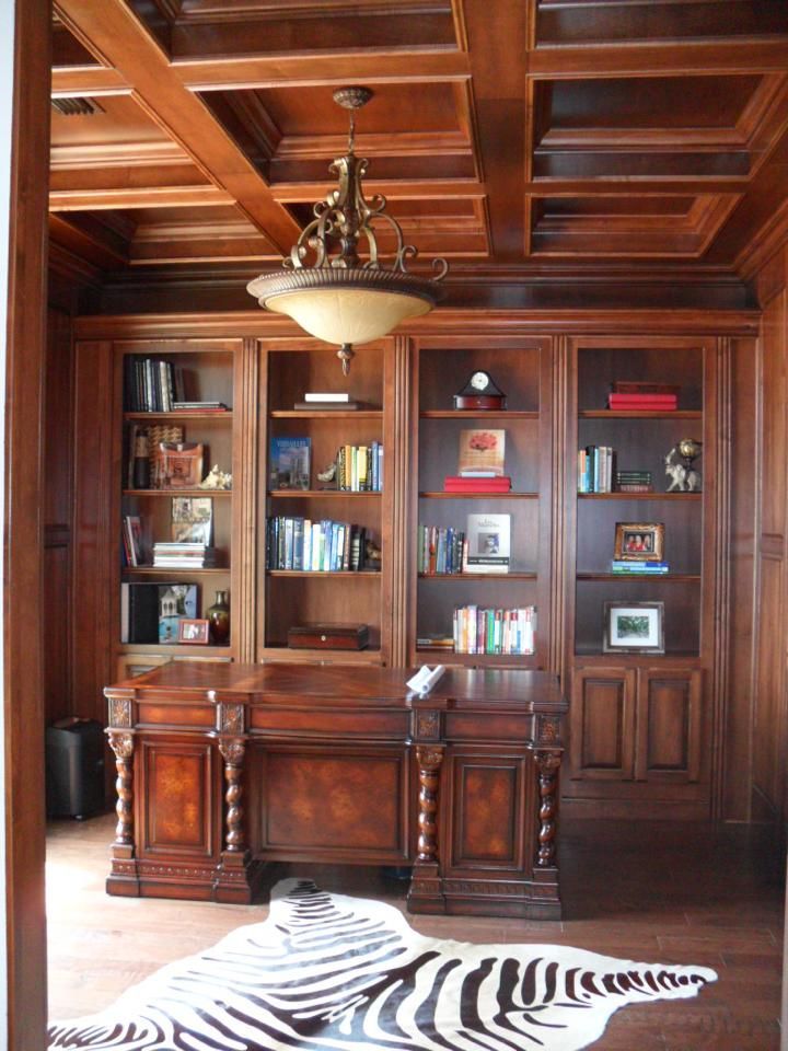 Wood-paneled library with built-in shelves, chandelier, and zebra rug on the floor.