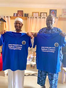 Two men holding blue t-shirts with text, indoors.