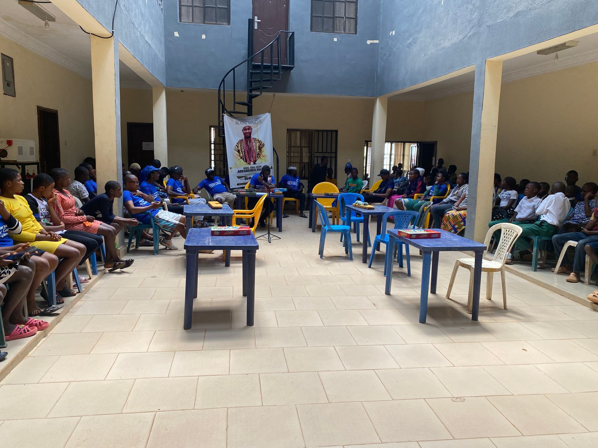 People seated at tables in an open-air building. A banner hangs above a table with people seated behind it.