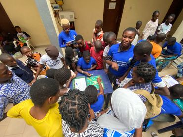 Group of people looking at materials on a table. Most wear blue shirts. Indoors, brightly lit.