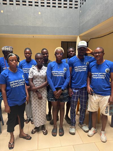 Group of people in blue shirts, posing indoors. Some wear caps; neutral expressions.
