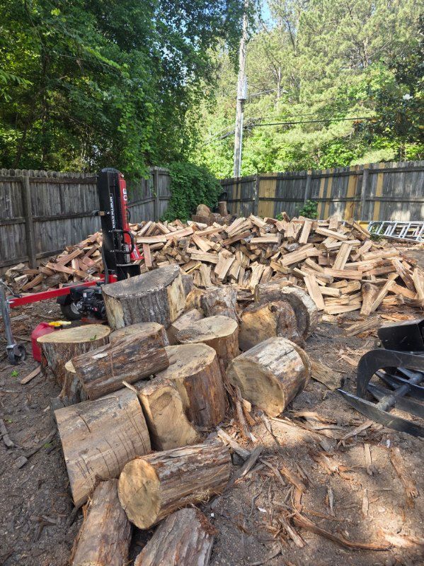 Split firewood piled in a fenced backyard with logs, wood chips, and a red wood splitter