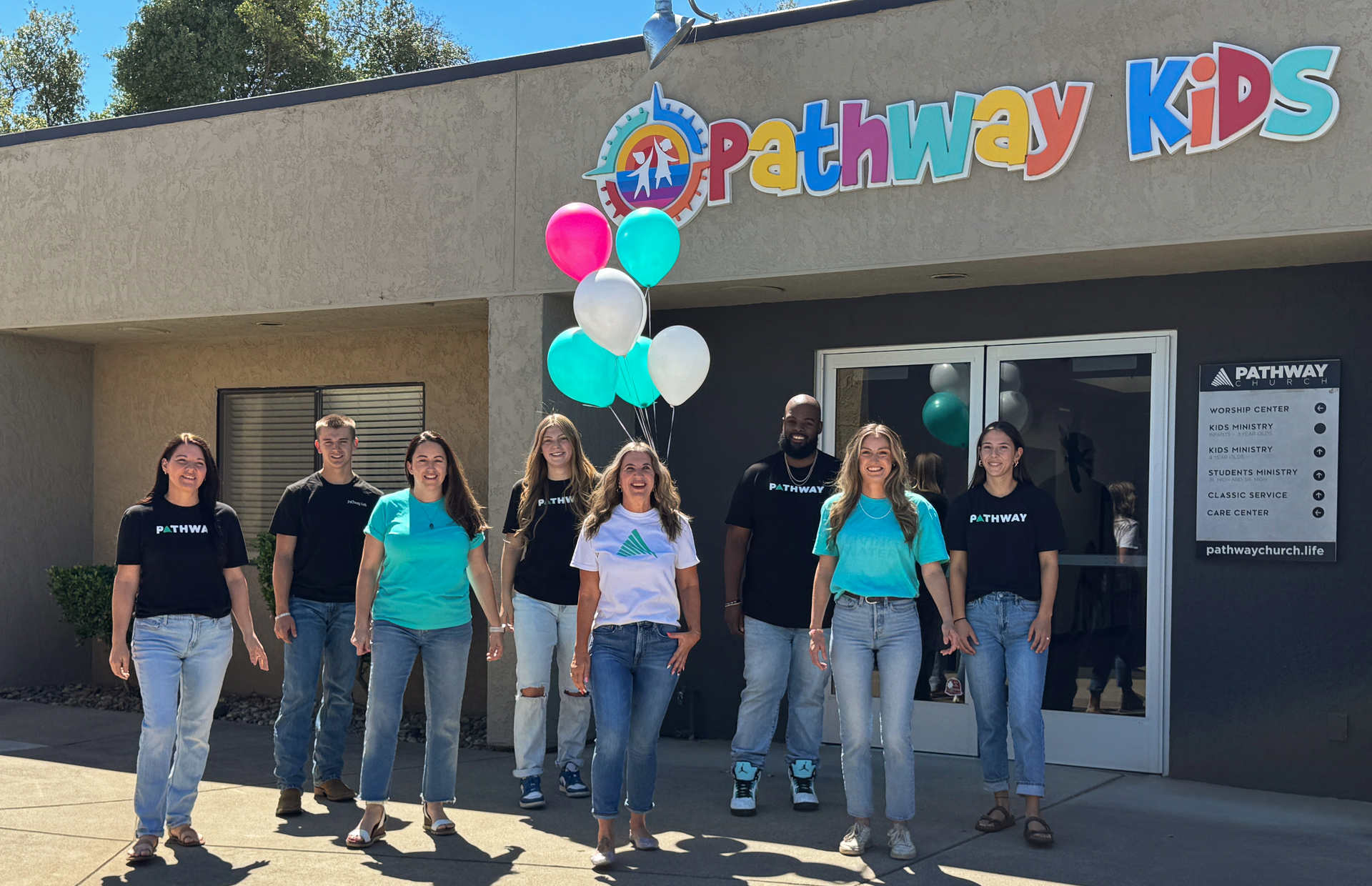 group of adults standing outside, one is holding a bunch of balloons