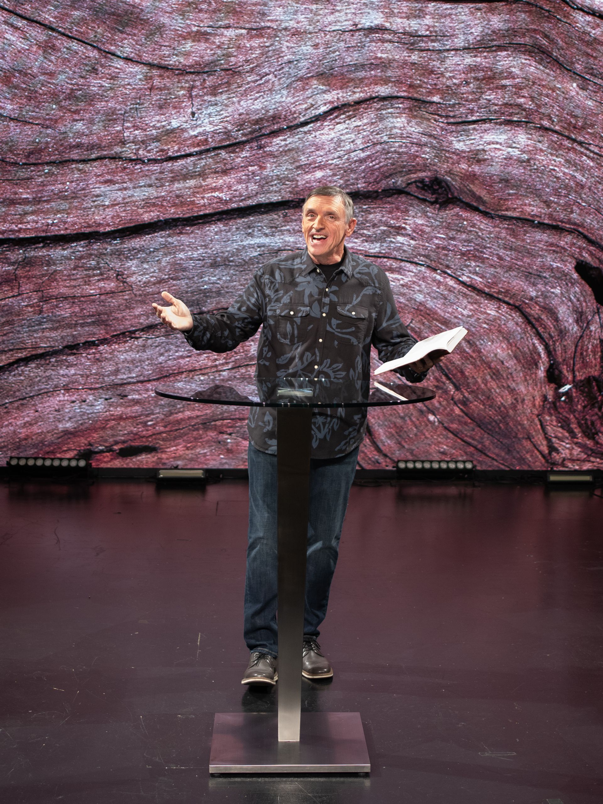 image of man standing on a stage, holding a Bible and talking