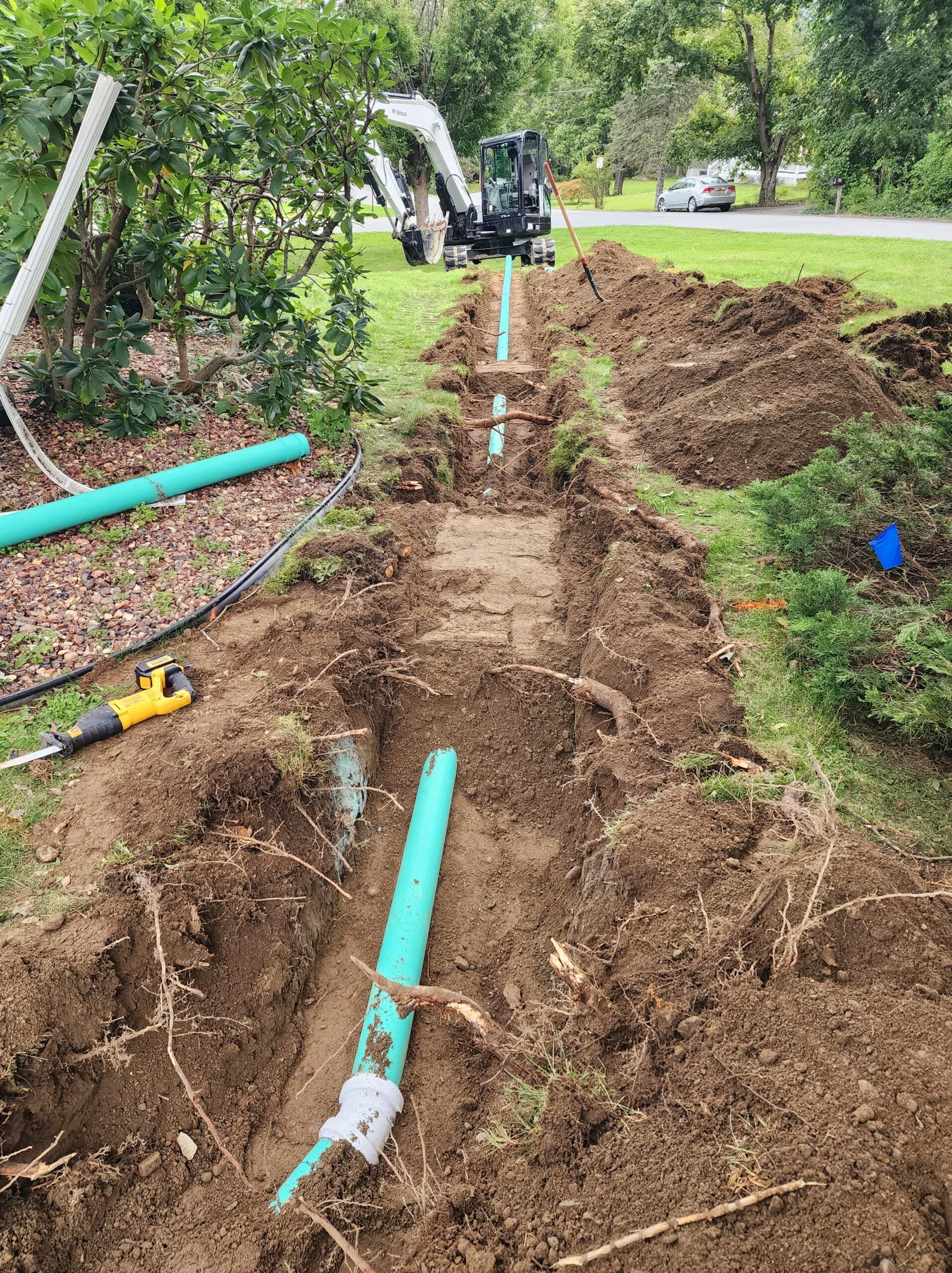 A green pipe is being installed in the dirt in a yard.