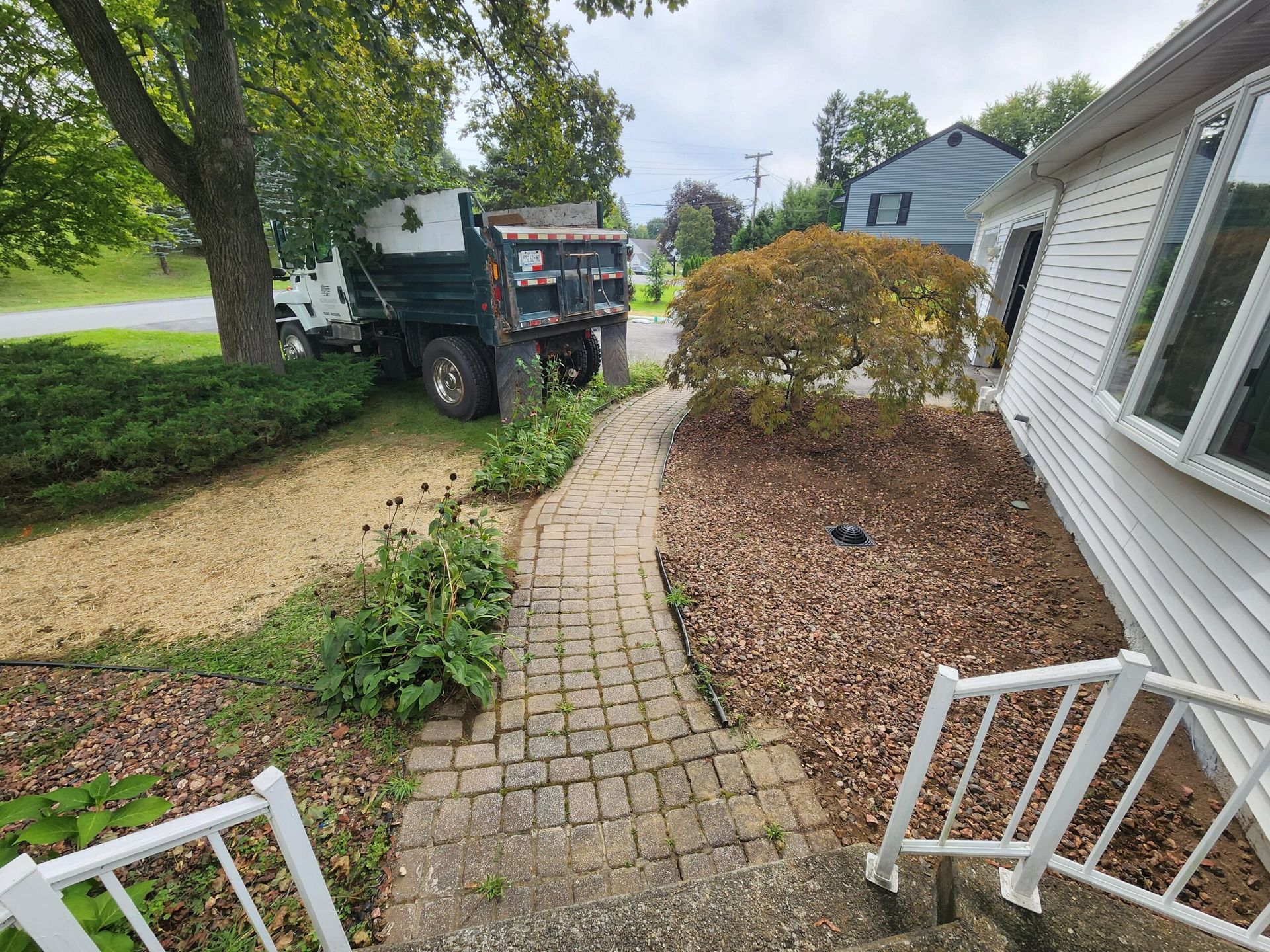 A dump truck is parked on the side of a brick walkway next to a house.