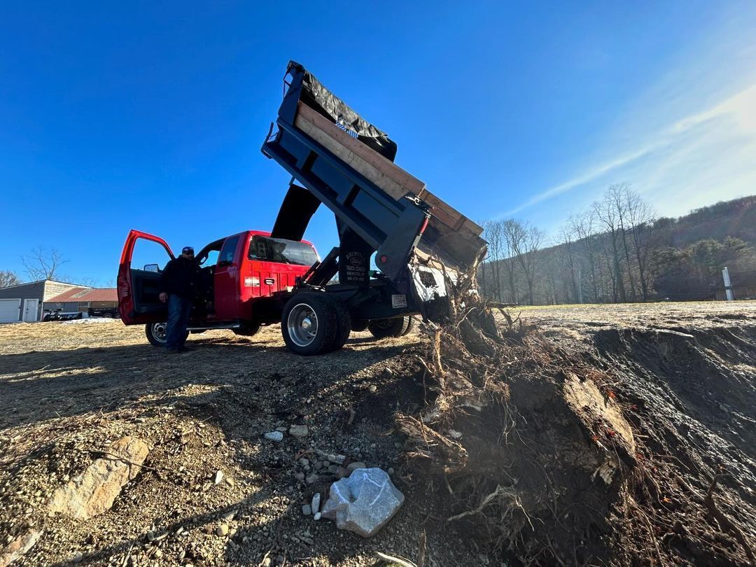 A red dump truck is sitting on top of a dirt field.