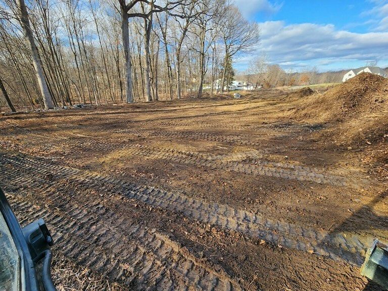 A tractor is driving through a dirt field with trees in the background.