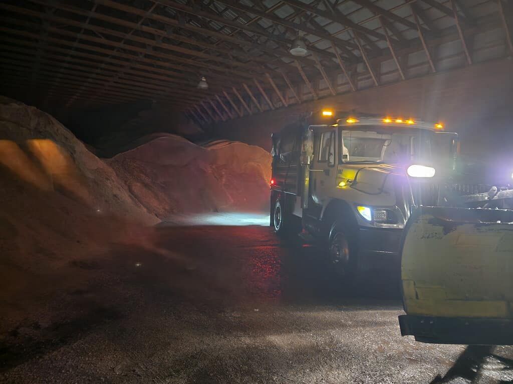 A snow plow is parked in a warehouse at night.