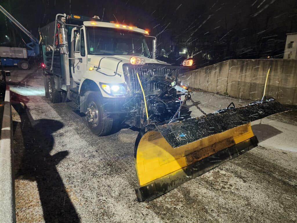 A snow plow is sitting on the side of a road at night.