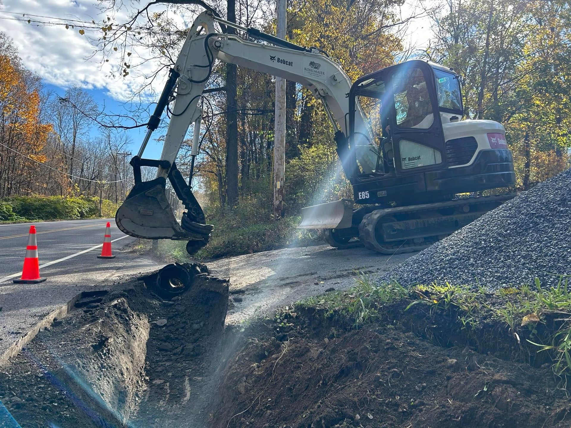 A small excavator is digging a hole in the side of a road.