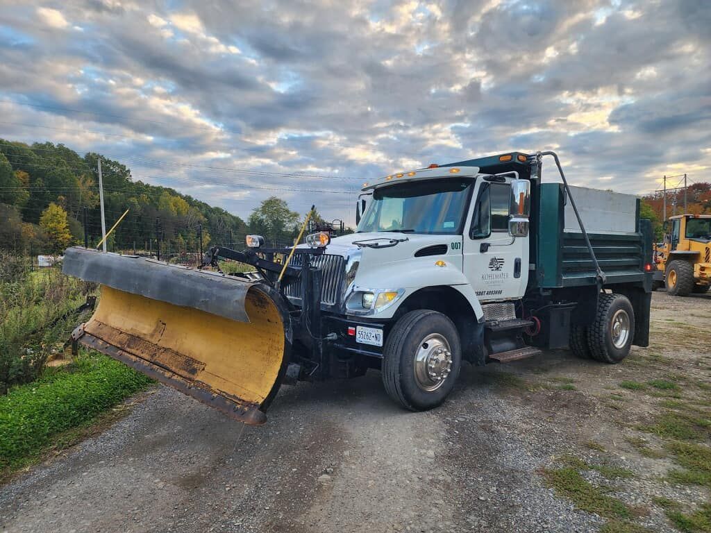 A snow plow truck is parked on the side of a dirt road.