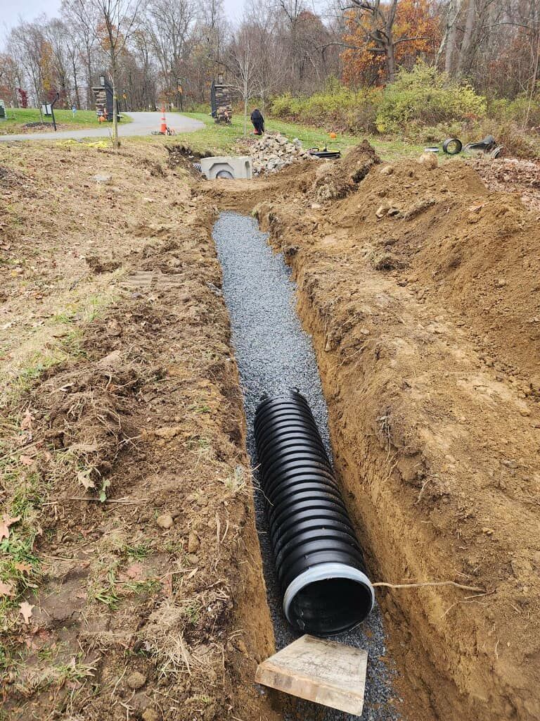 A large black pipe is being installed in a trench.