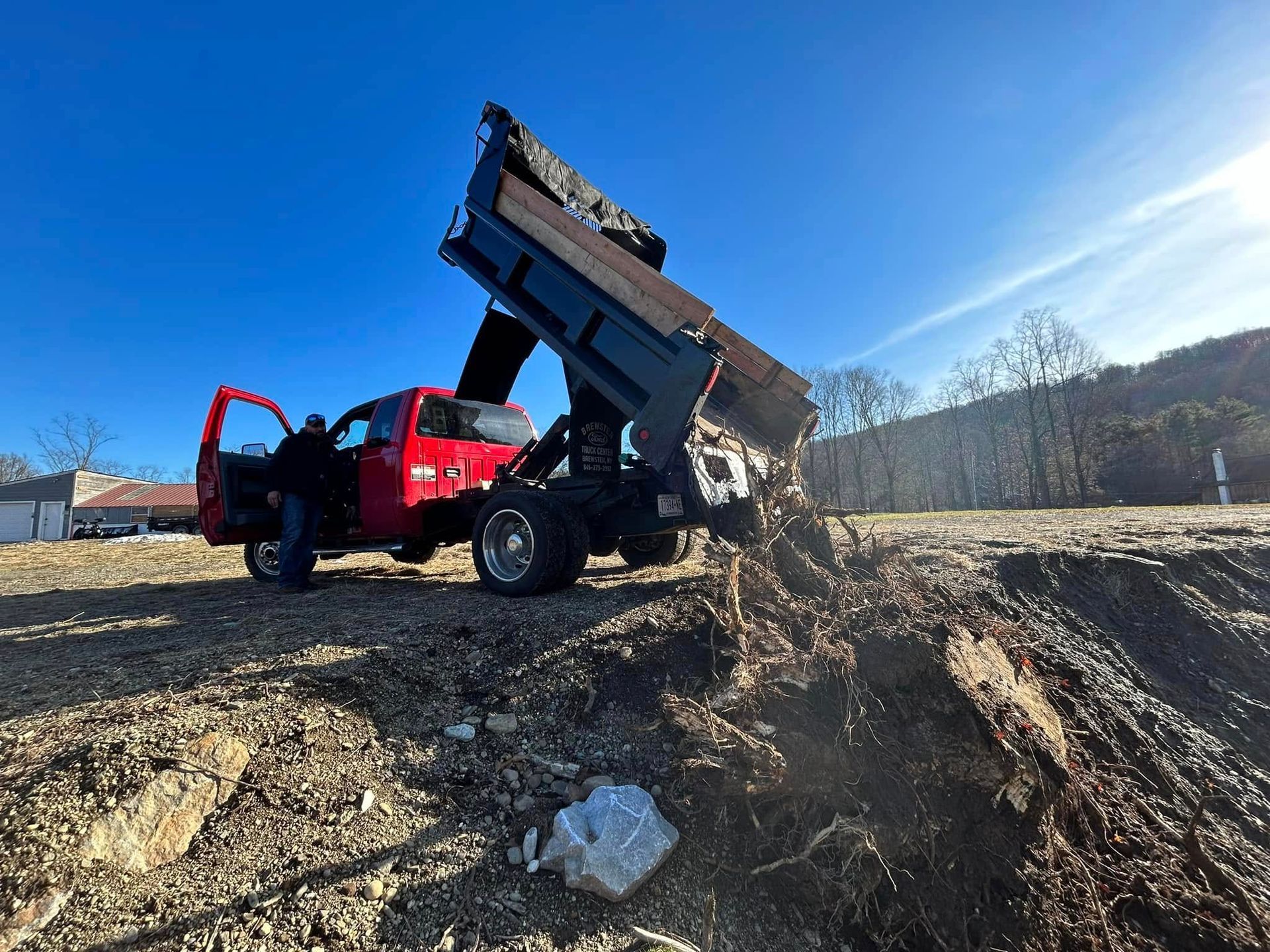 A red truck is loading dirt into a dumpster.