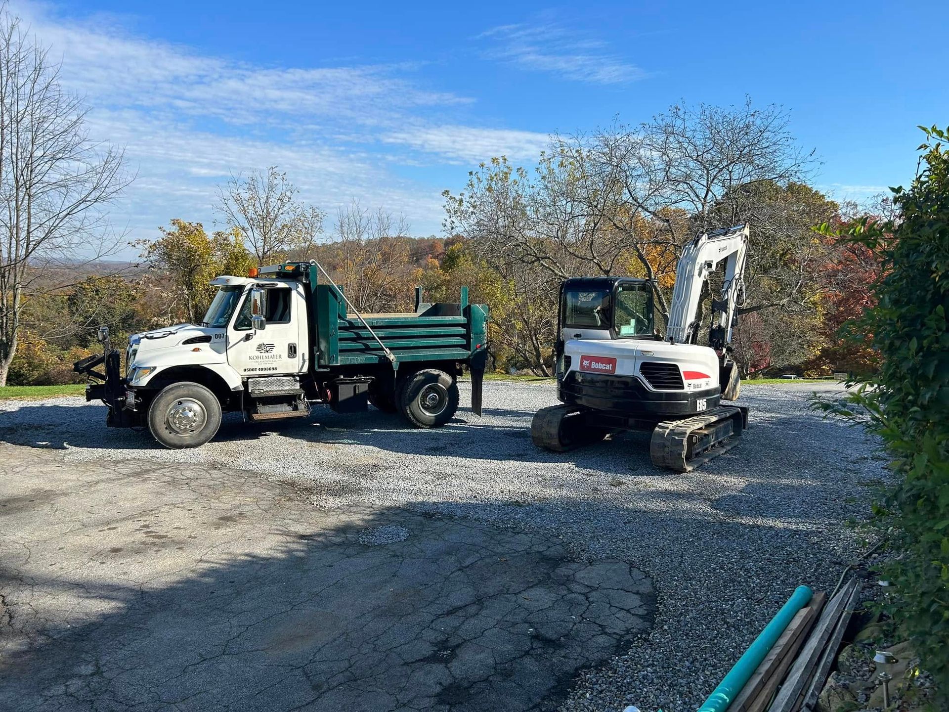 A dump truck and an excavator are parked in a gravel lot.