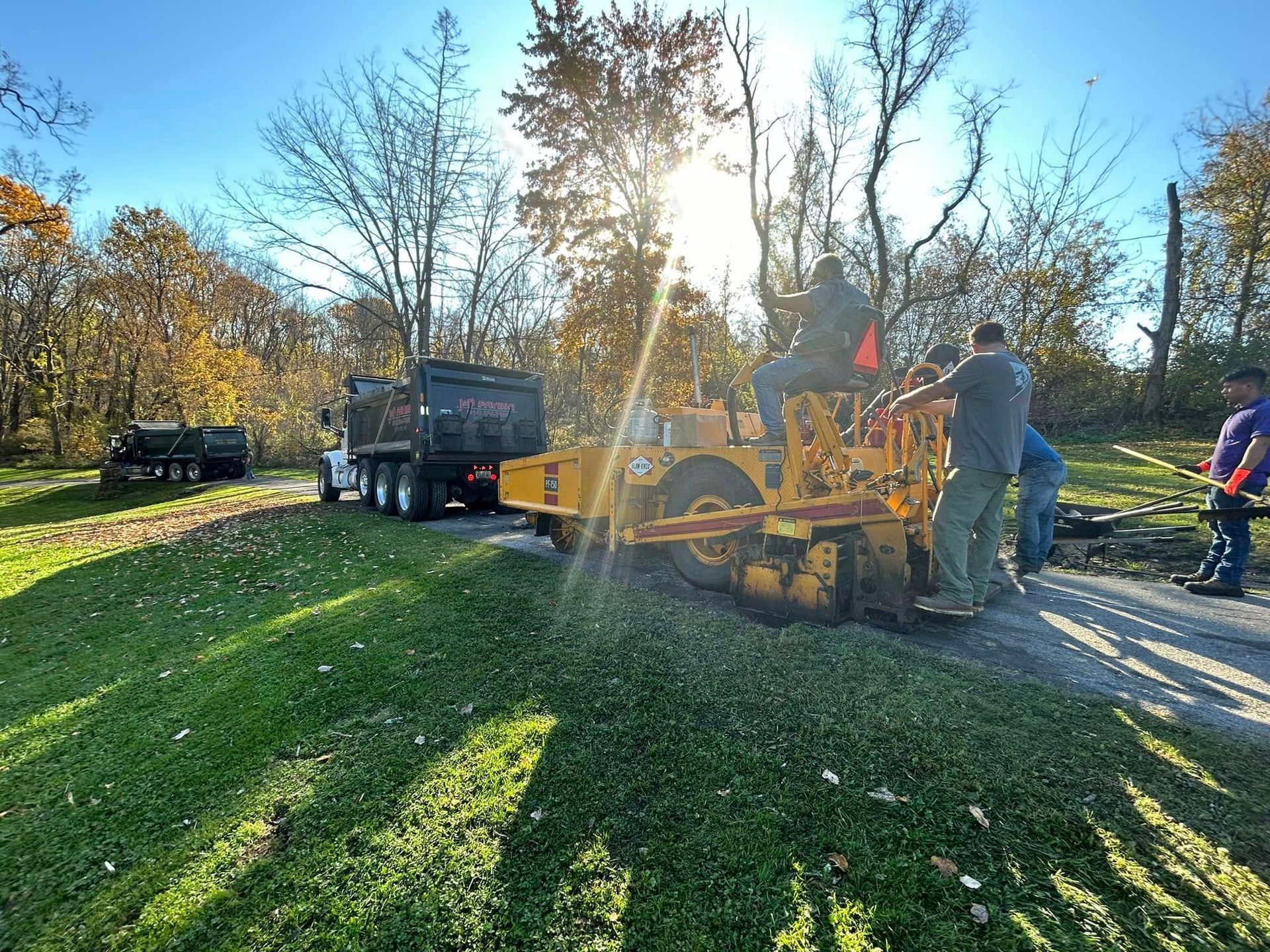 A group of men are standing next to a yellow tractor on the side of a road.