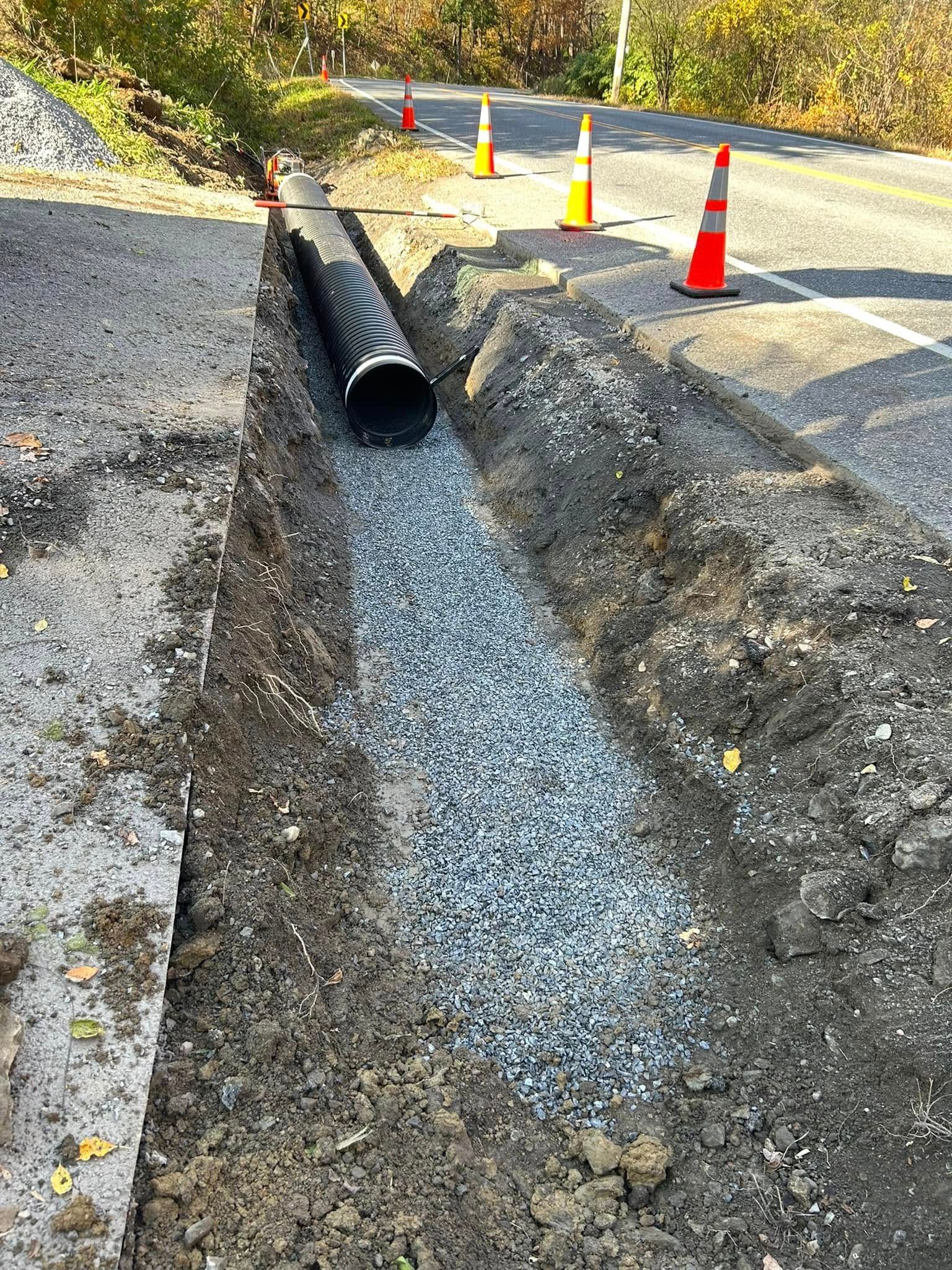 A large pipe is being installed in a trench next to a road.