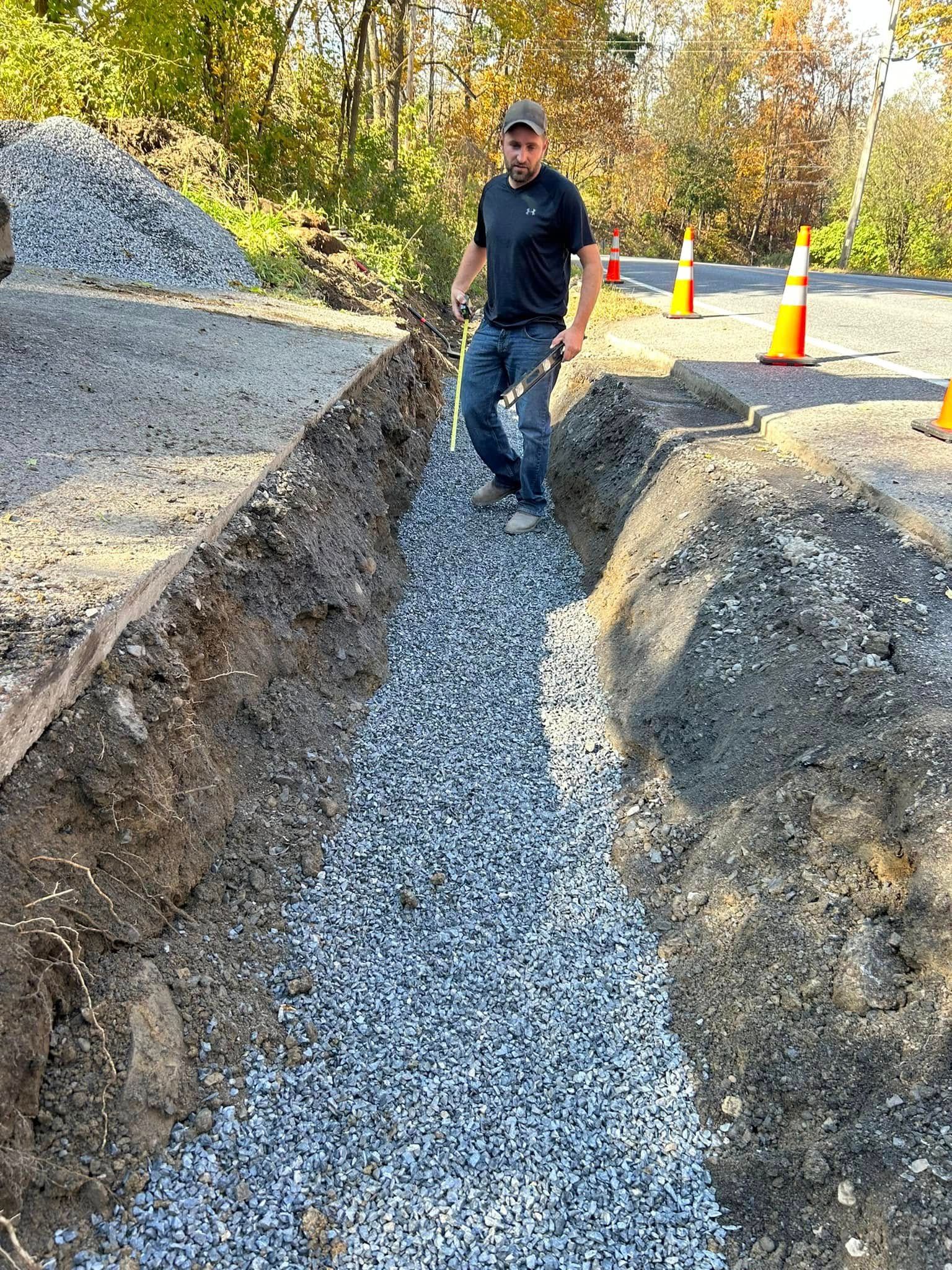 A man is standing in a trench next to a pile of gravel.
