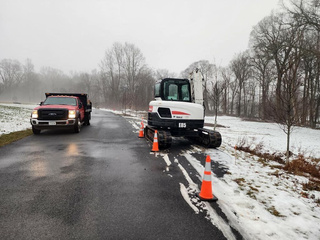 A truck and a bulldozer are parked on the side of a snowy road.