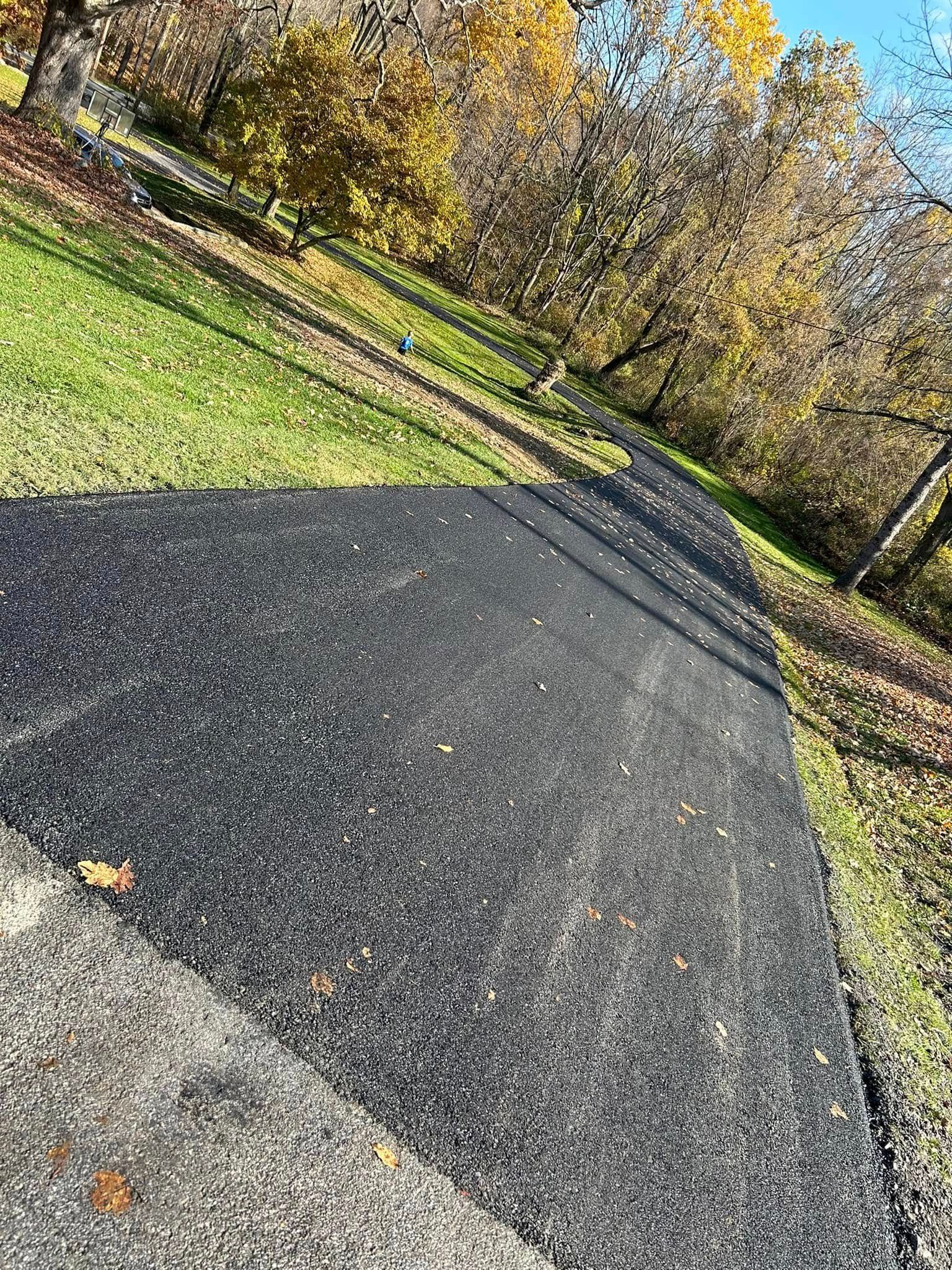 A black asphalt road going through a park with trees in the background.