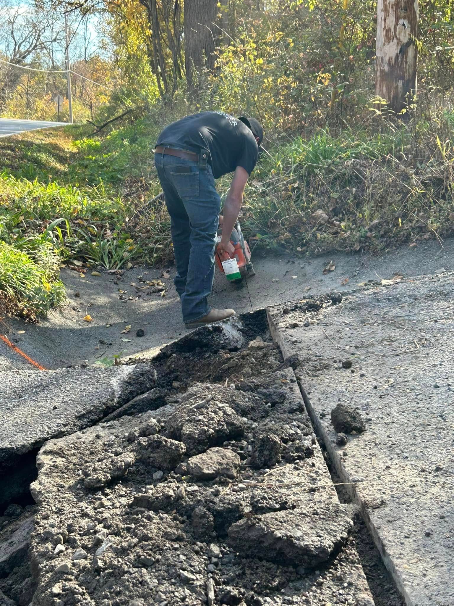 A man is digging in the dirt on the side of a road.