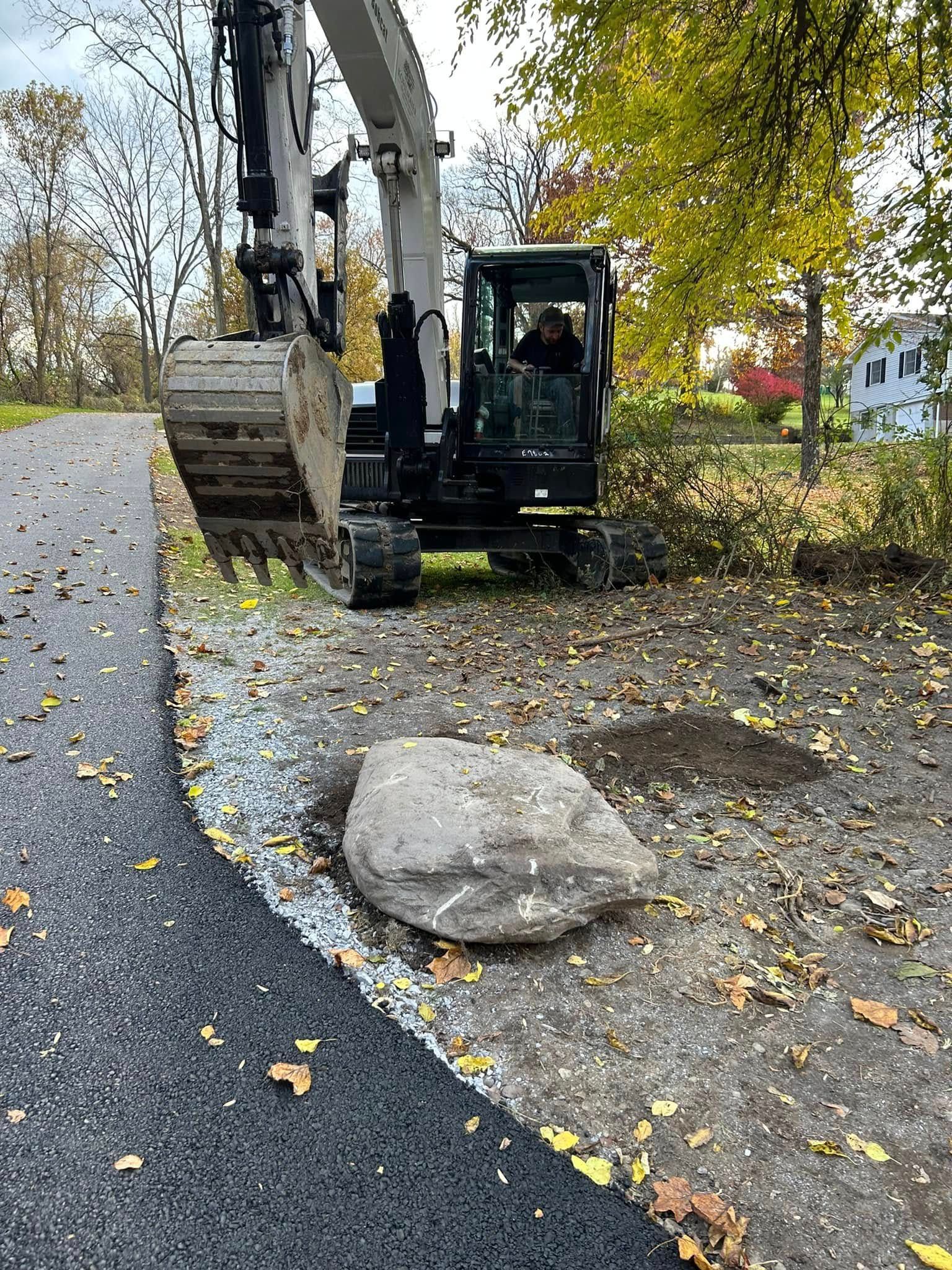 A large rock is sitting on the side of a road next to an excavator.