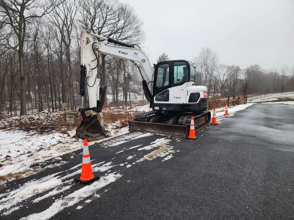 A white excavator is parked on the side of a snowy road.