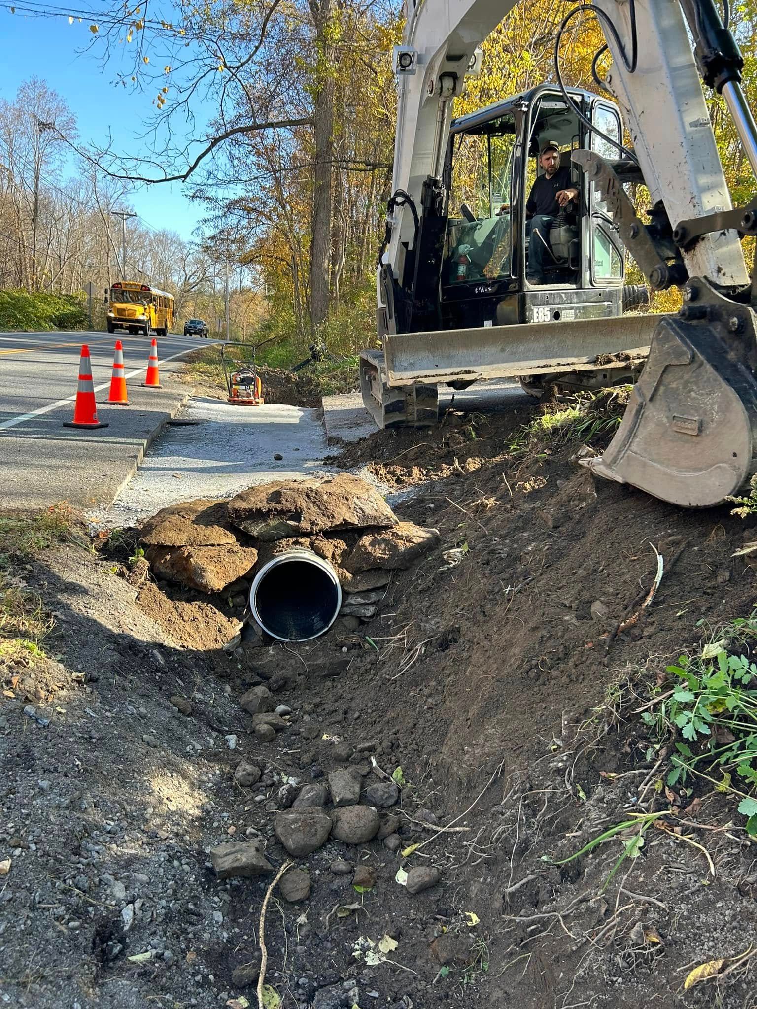 A man is driving a bulldozer on a dirt road next to a pipe.