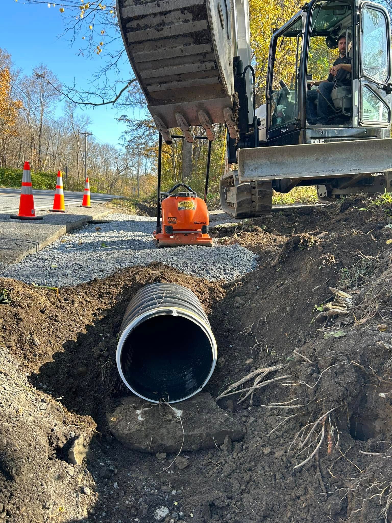 A man is driving a bulldozer next to a large pipe in the dirt.