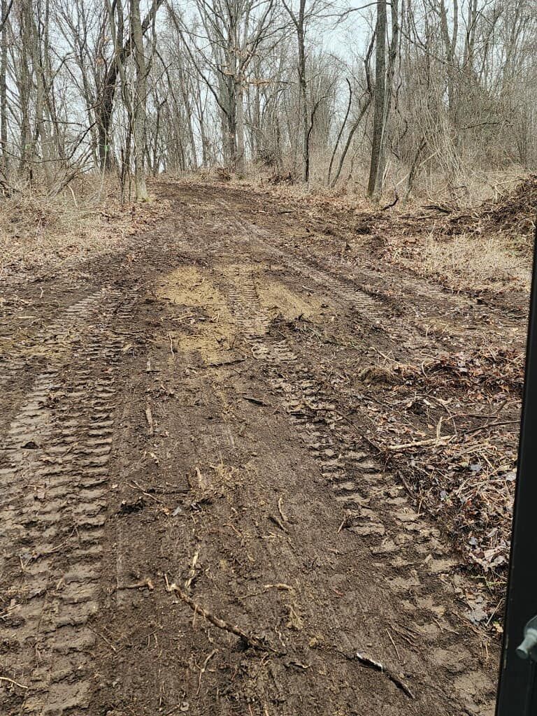 A tractor is driving down a dirt road in the woods.