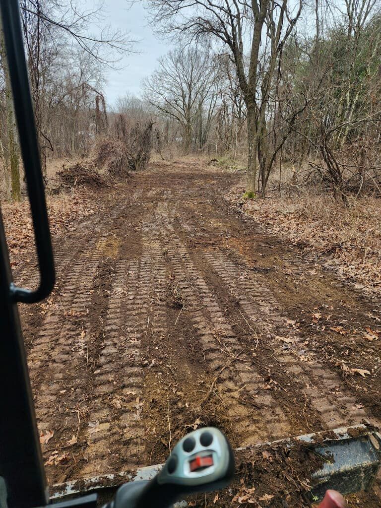 A tractor is driving down a dirt road in the woods.