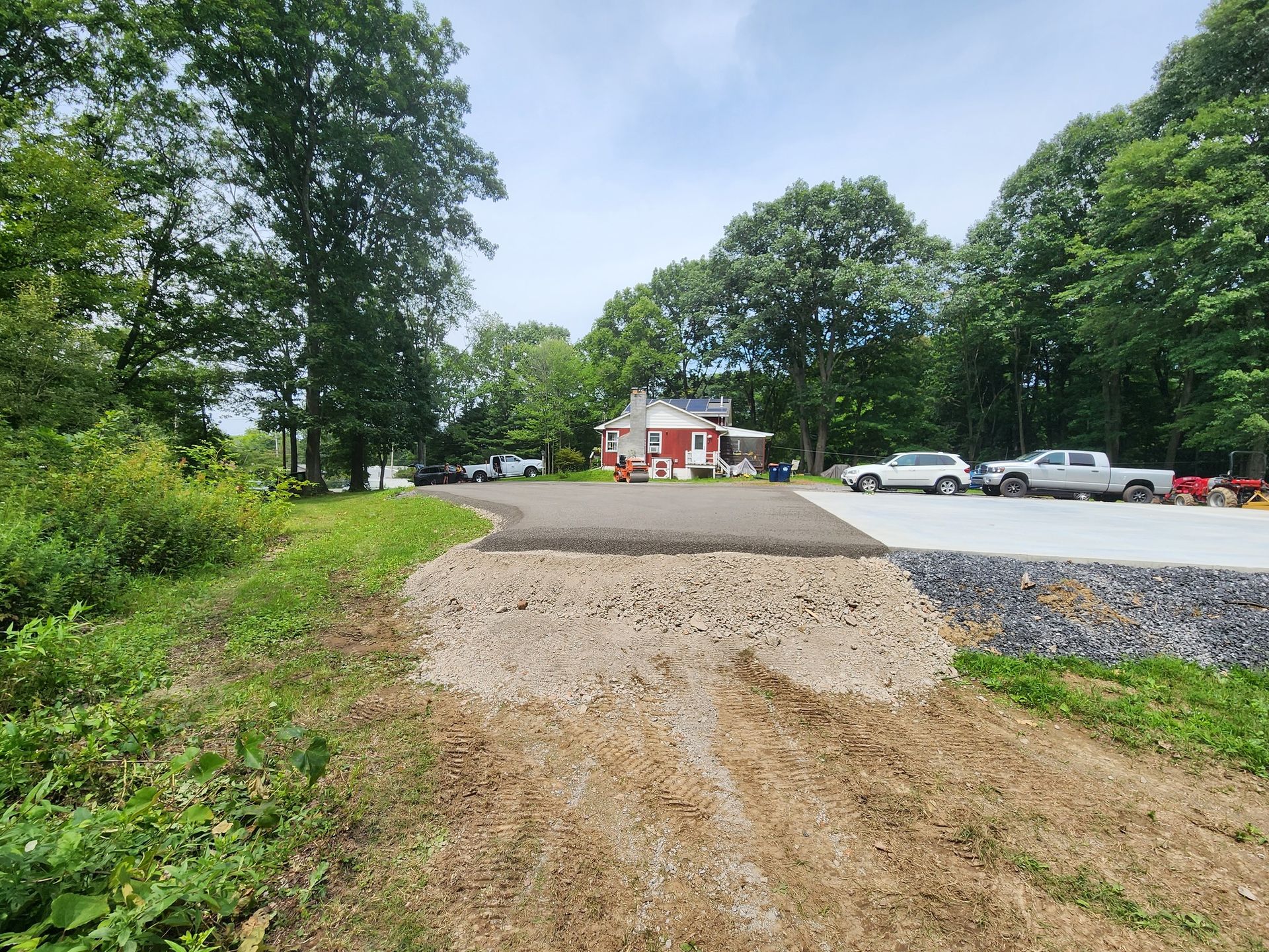 A dirt road leads to a parking lot with a red house in the background.