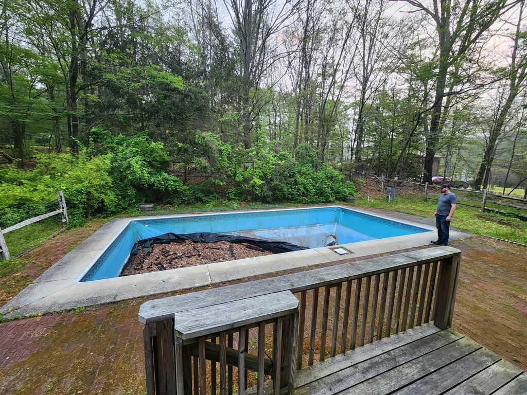 A man is standing next to a swimming pool in the middle of a forest.