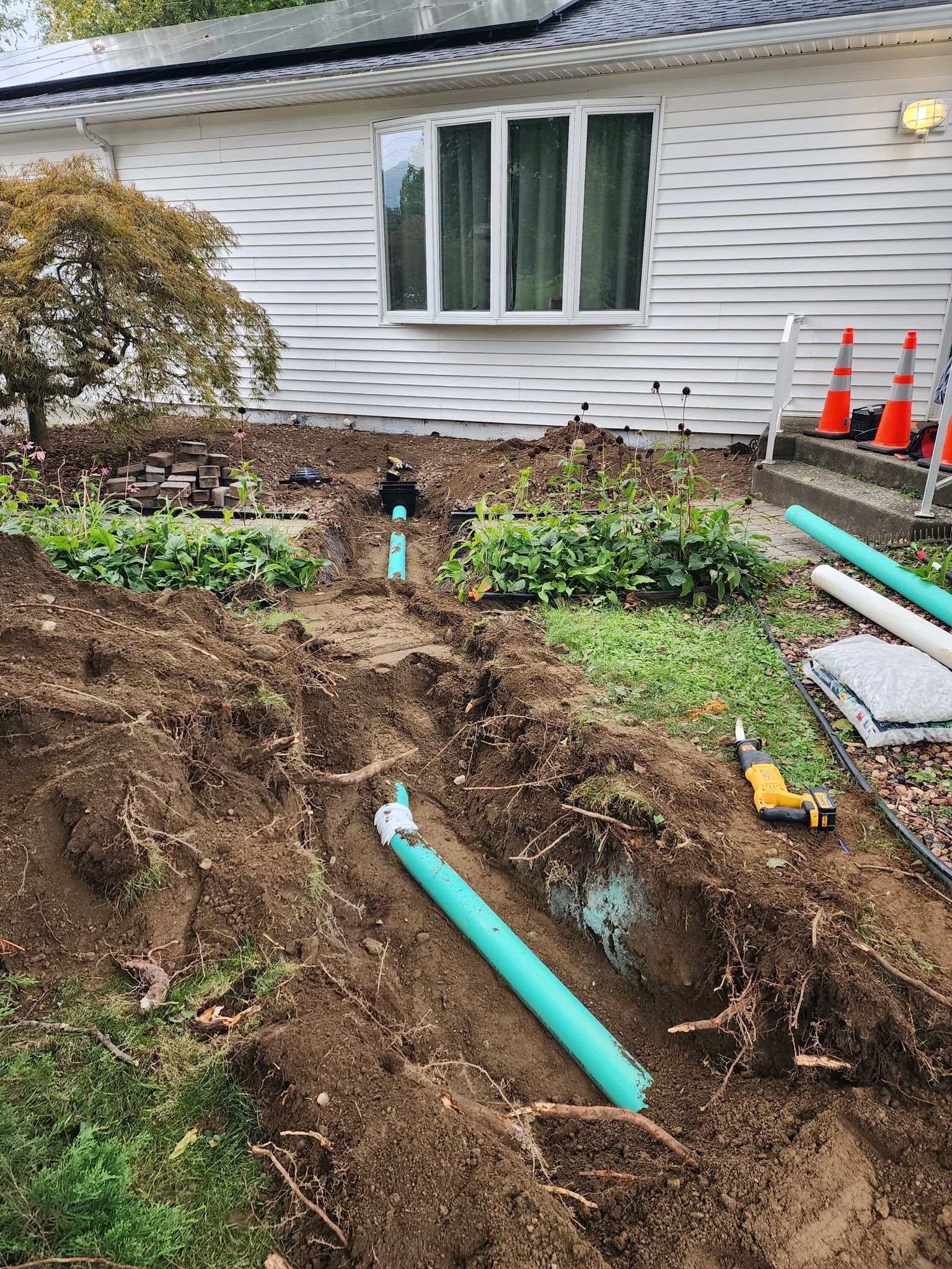 A white house with a lot of pipes in the dirt in front of it.
