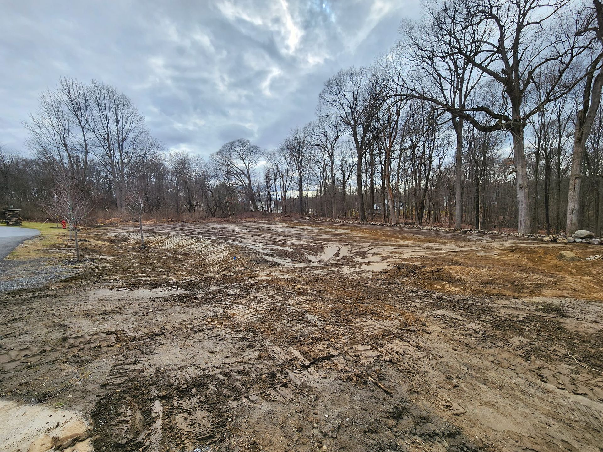 A muddy field with trees in the background and a road in the foreground.