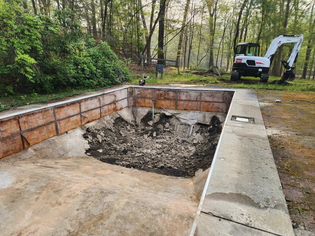 An excavator is digging a hole in the ground next to a swimming pool.