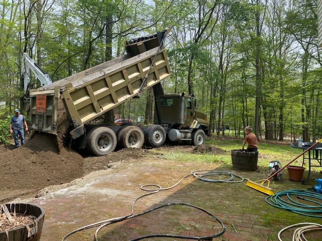 A dump truck is being loaded with dirt in a driveway.