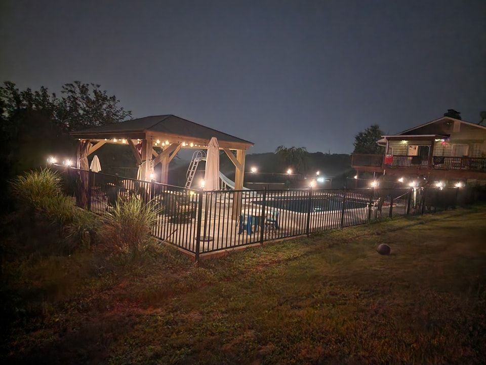 A gazebo is lit up at night next to a swimming pool.