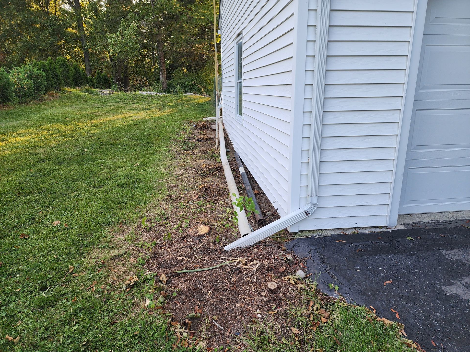 A white house with a garage and a drain pipe on the side of it.