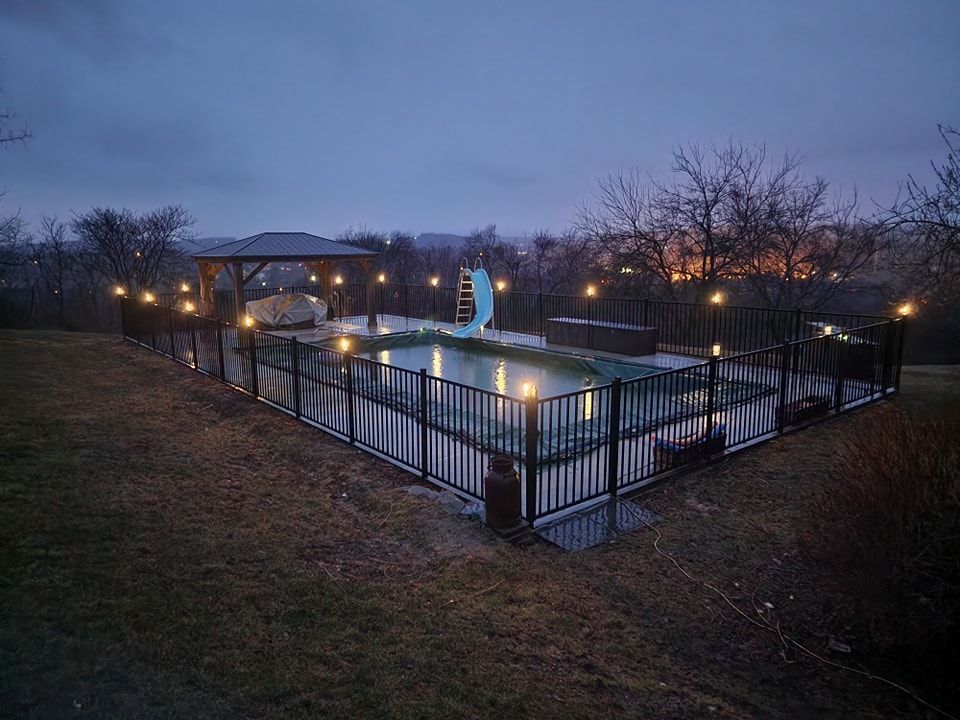 A large swimming pool is surrounded by a fence and lit up at night.