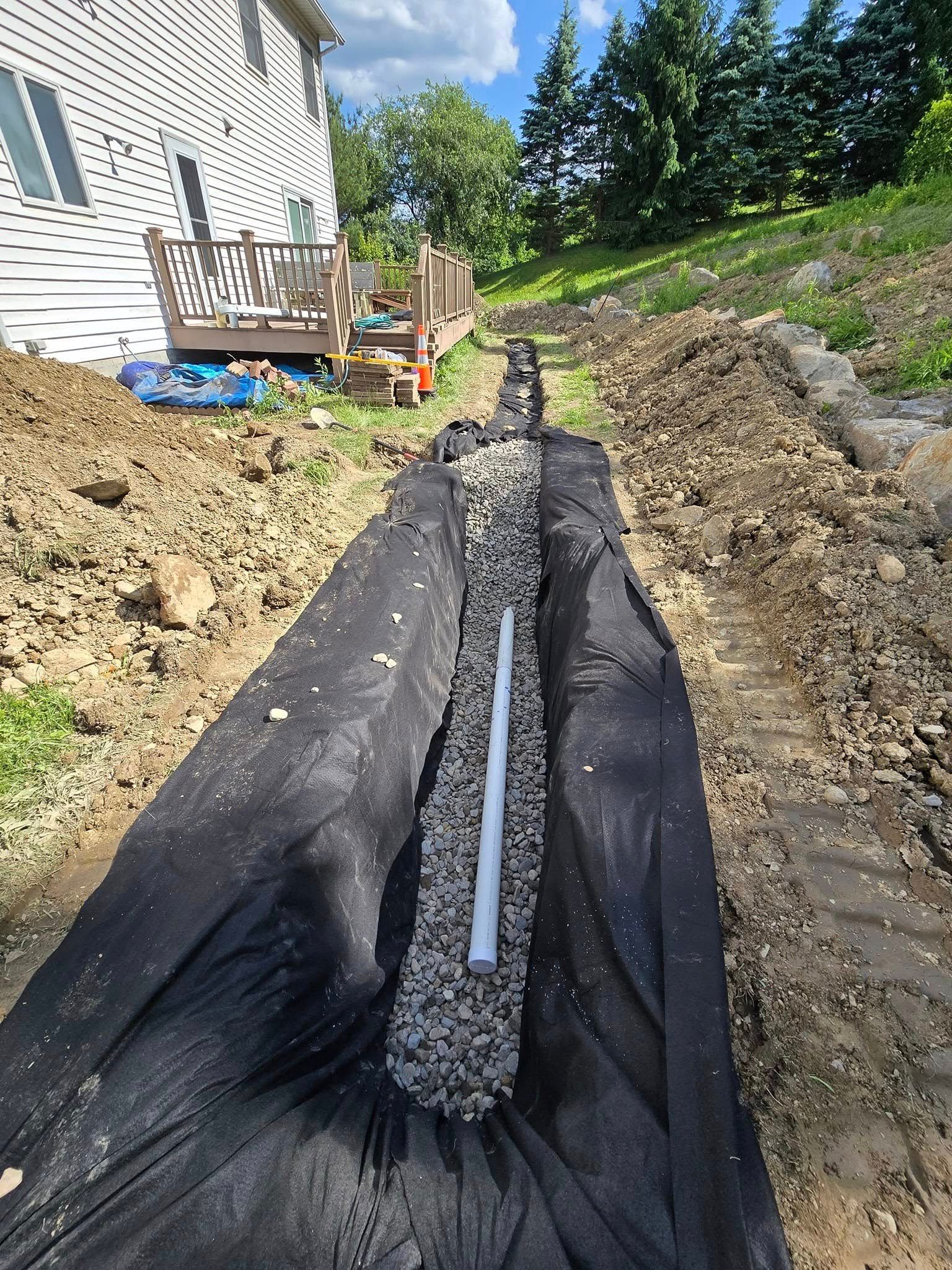 A pipe is laying in the dirt next to a house.