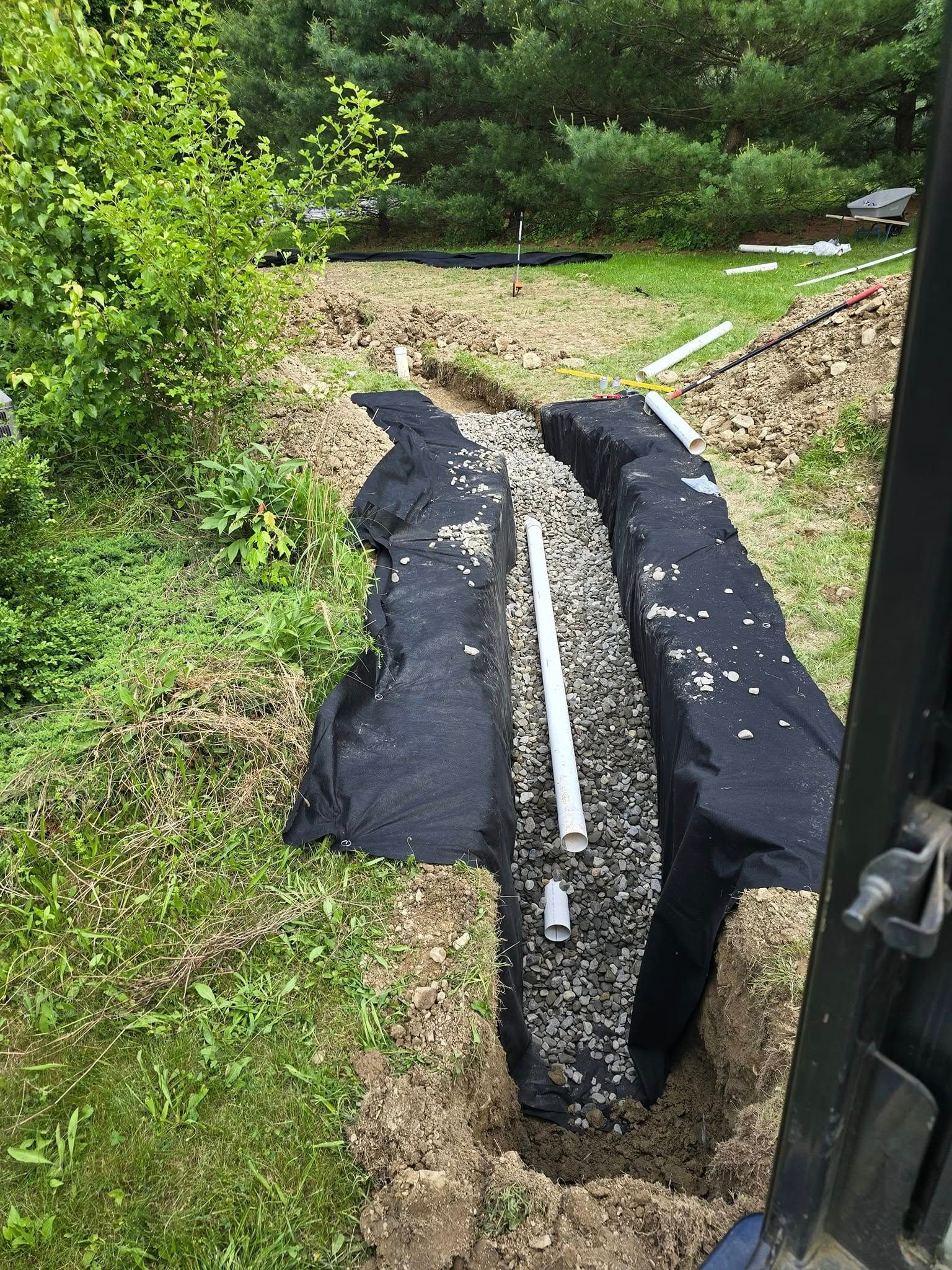 A forklift is digging a hole in the ground to install a drainage system.