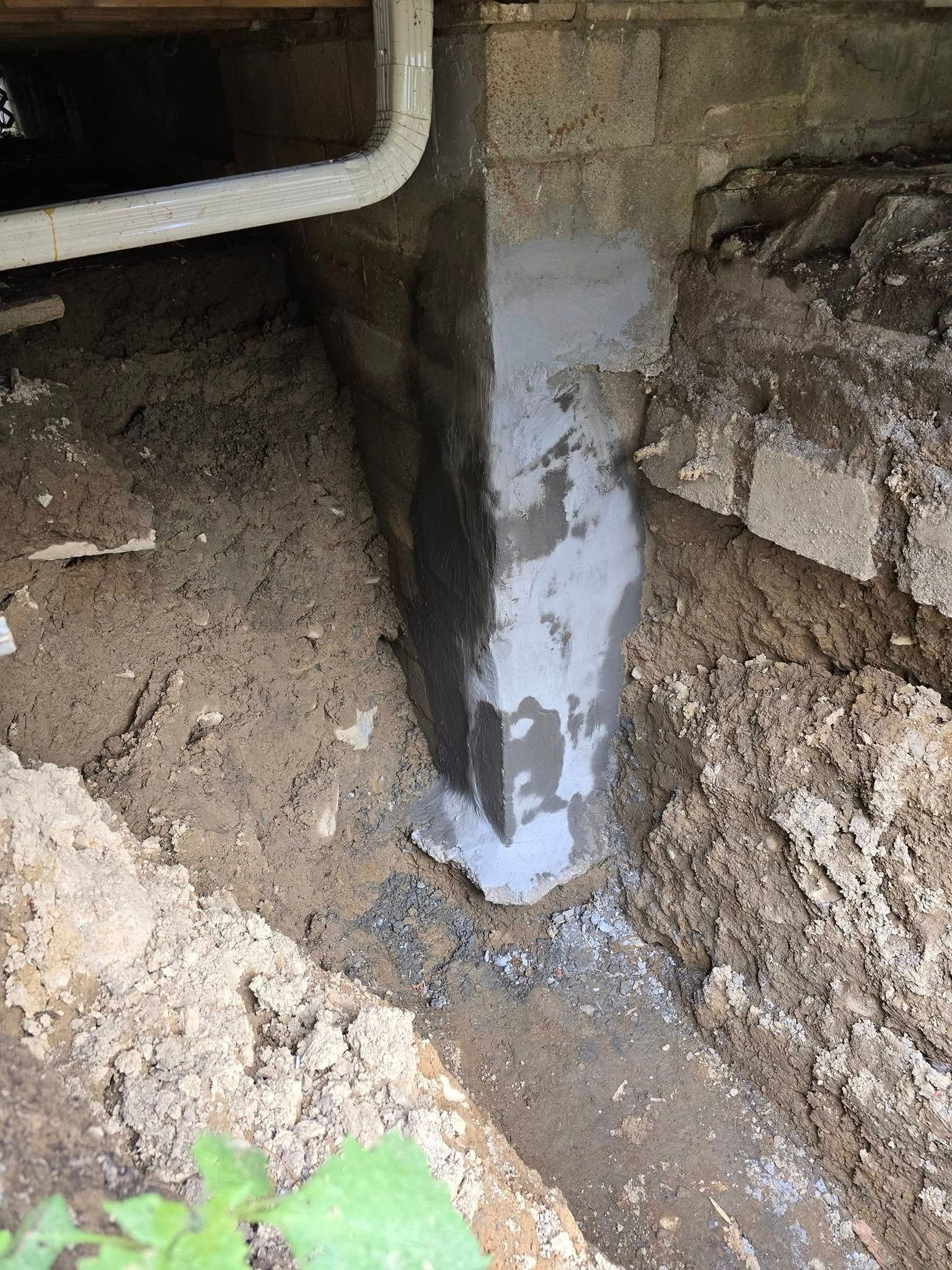 A concrete pillar is sitting in the dirt next to a brick wall.