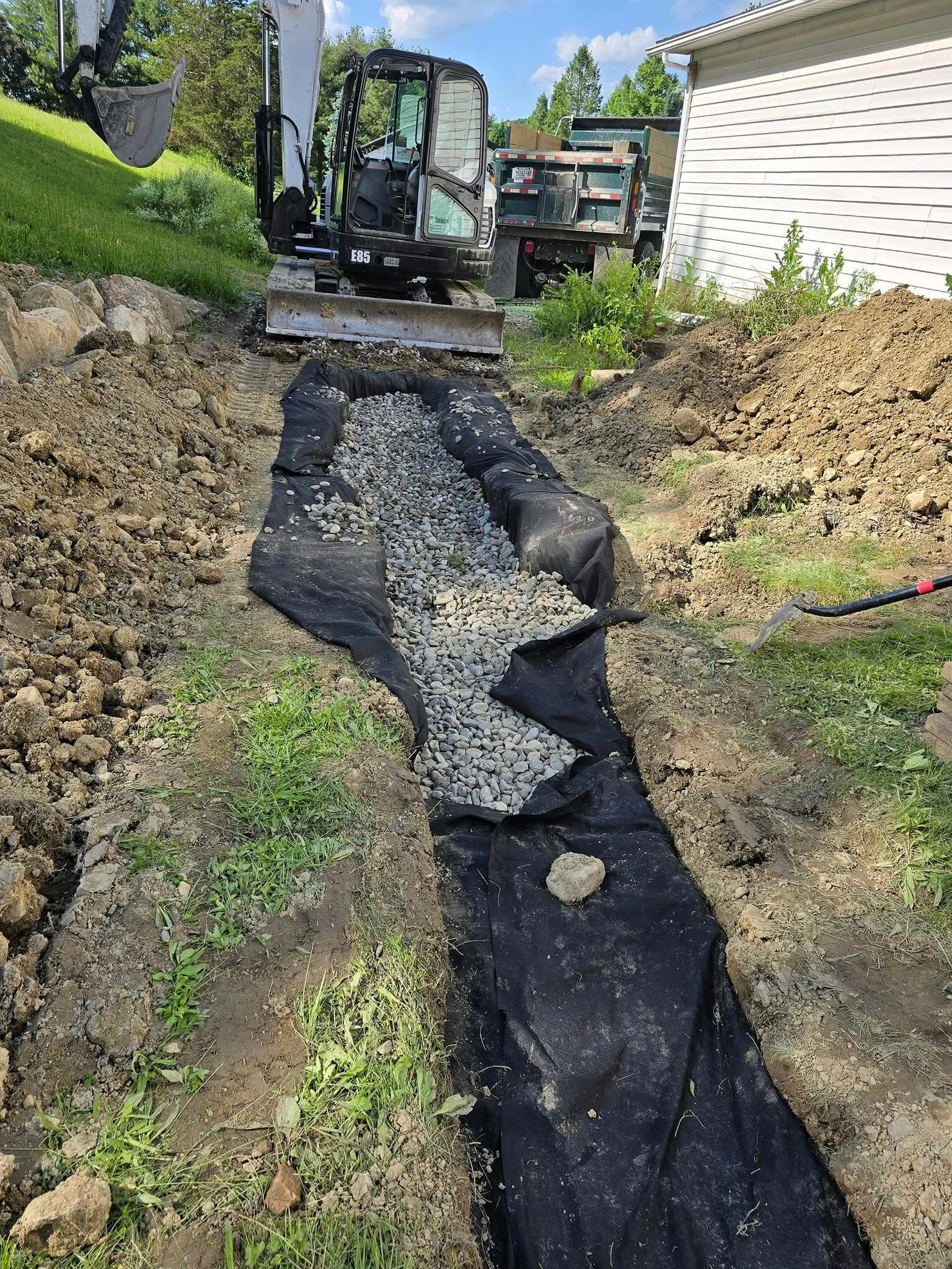 A bulldozer is digging a trench in the dirt in front of a house.