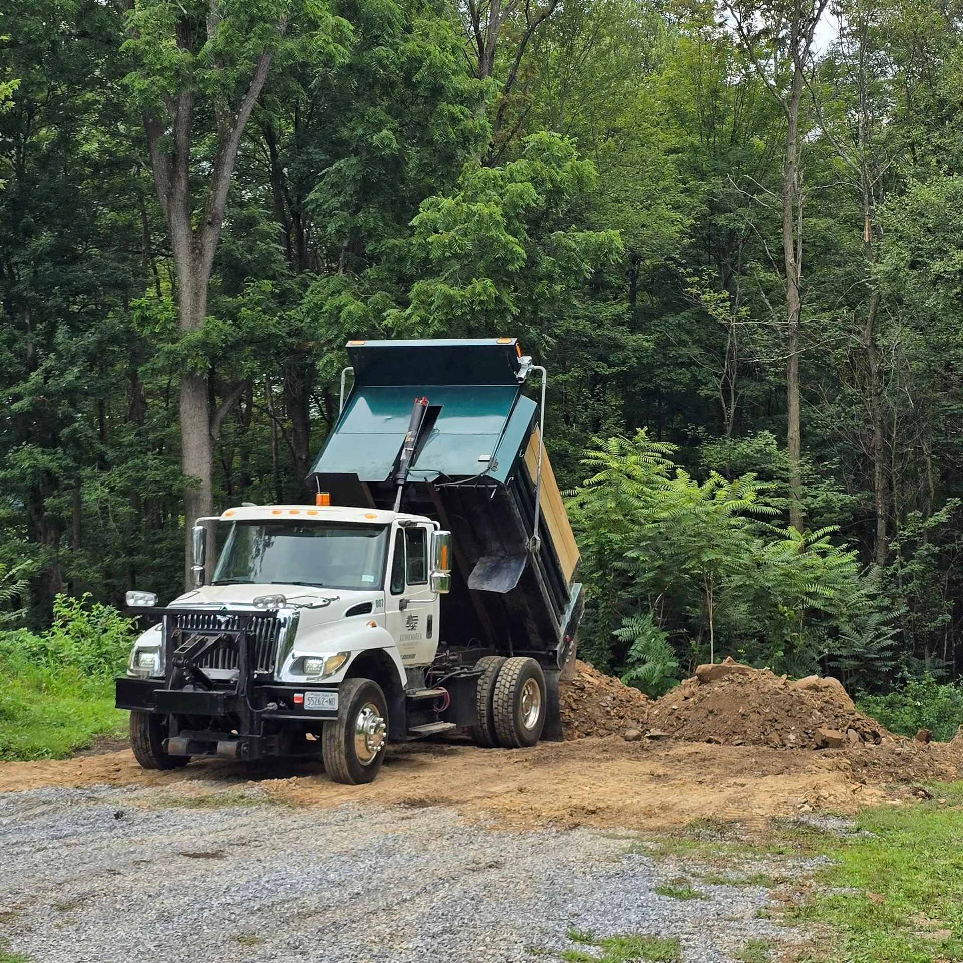 A dump truck is driving down a dirt road in the woods.