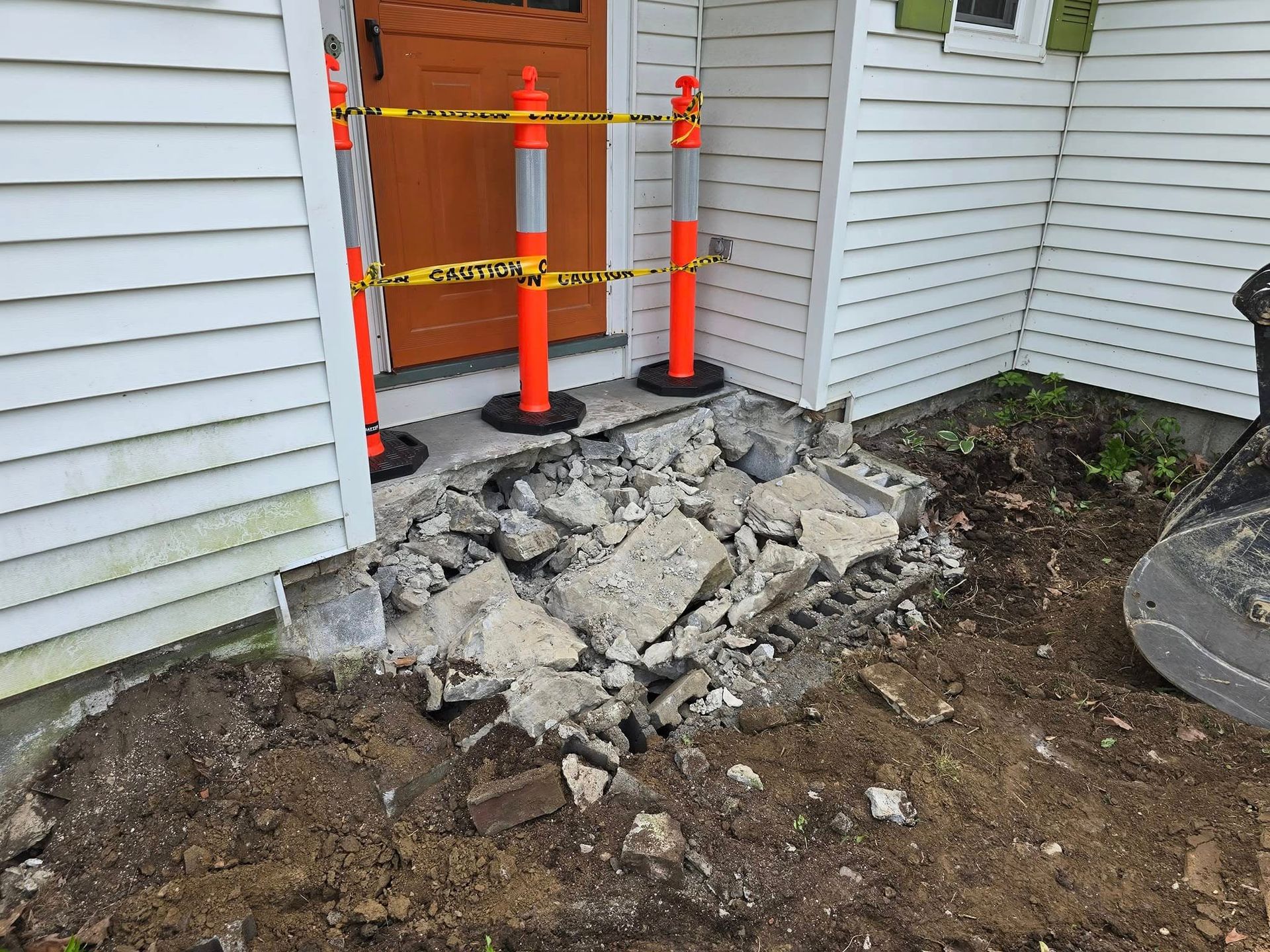 A concrete walkway is being demolished in front of a house.