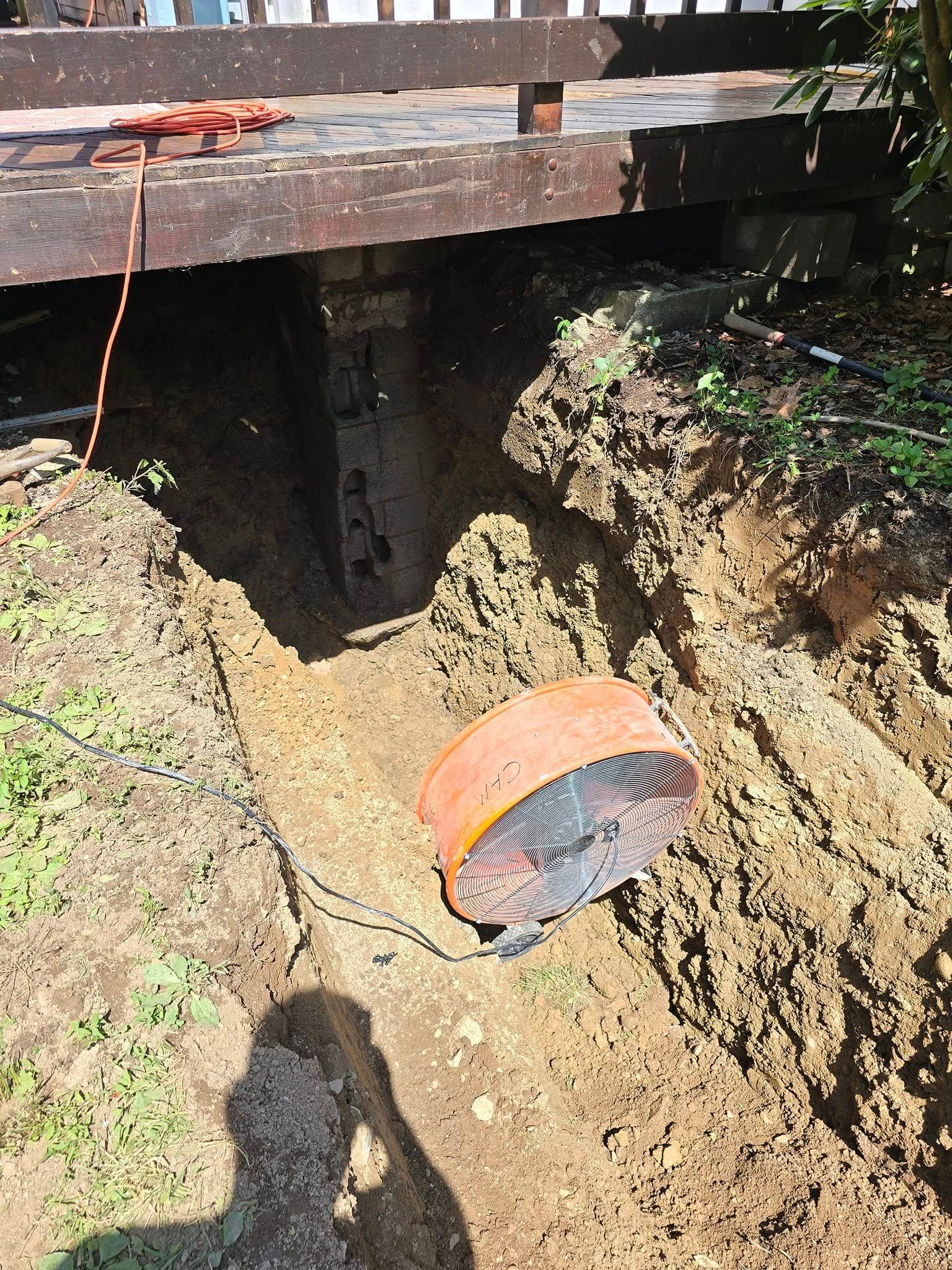 A fan is sitting in the dirt next to a wooden deck.