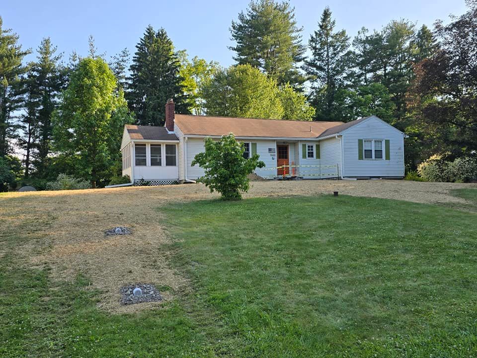 A white house with a brown roof is surrounded by trees